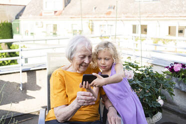 Granddaughter showing mobile phone to grandmother in balcony - SVKF00296