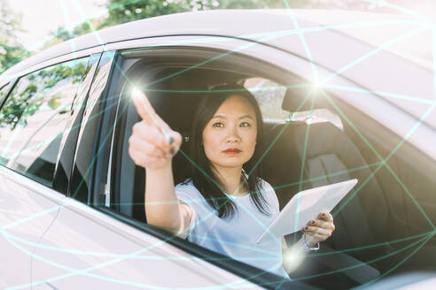 Geschäftsfrau mit Tablet-PC, die Linien und Punkte auf einem virtuellen Bildschirm im Auto verbindet - MEUF06469