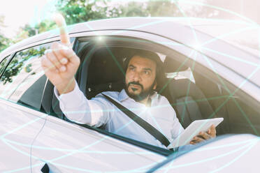 Mature man using tablet PC on virtual screen sitting in car - MEUF06471