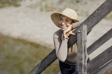 Smiling woman wearing hat leaning on railing - AANF00262