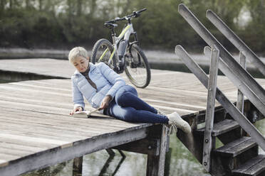 Reife Frau liest Buch auf dem Pier liegend - AANF00271