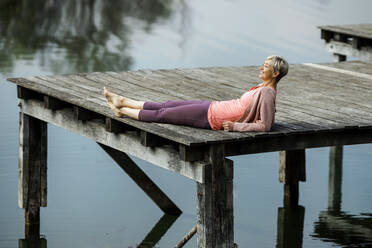 Smiling mature woman lying on pier by lake - AANF00295