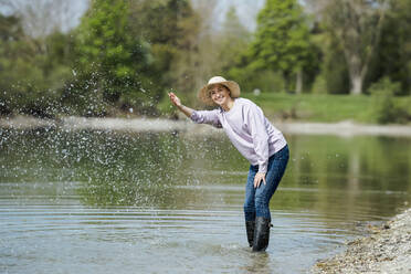 Glückliche reife Frau spritzt Wasser und genießt am See - AANF00296