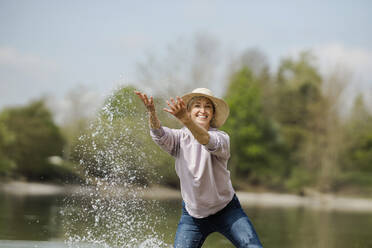 Fröhliche reife Frau spielt mit Wasser an einem sonnigen Tag - AANF00299