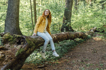 Junge Frau sitzt auf einem umgestürzten Baumstamm im Wald - VPIF06524