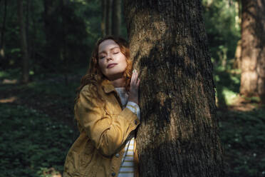 Junge Frau mit geschlossenen Augen umarmt Baum im Wald - VPIF06527