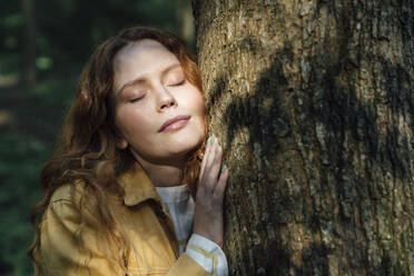 Woman with eyes closed embracing tree in forest - VPIF06528