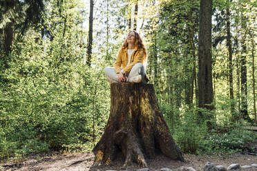 Frau sitzt im Schneidersitz auf einem Baumstumpf im Wald - VPIF06530