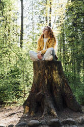 Junge Frau mit geschlossenen Augen sitzt auf einem Baumstumpf im Wald - VPIF06531