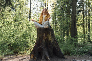 Junge Frau meditiert auf einem Baumstumpf im Wald - VPIF06532