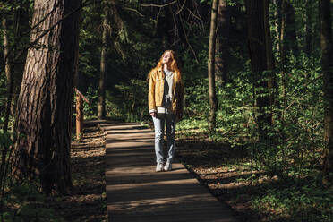 Young woman with eyes closed walking on footpath in forest - VPIF06536