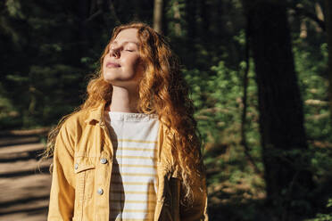 Woman with eyes closed enjoying sunlight in forest - VPIF06537