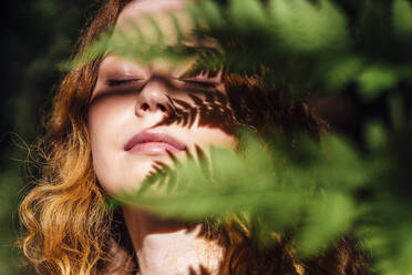 Woman with leaf shadow on face enjoying sunlight - VPIF06549