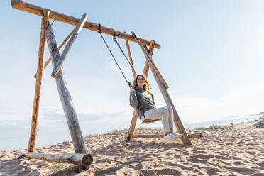 Young woman swinging on swing at beach - VPIF06555