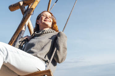 Smiling woman swinging on swing in front of sky - VPIF06556