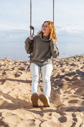 Young woman sitting on swing at beach - VPIF06557