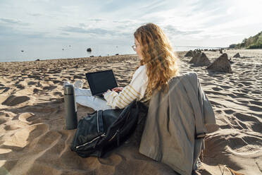 Junge Frau benutzt Laptop am Strand an einem sonnigen Tag - VPIF06574
