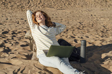 Frau mit Laptop entspannt am Strand an einem sonnigen Tag - VPIF06576