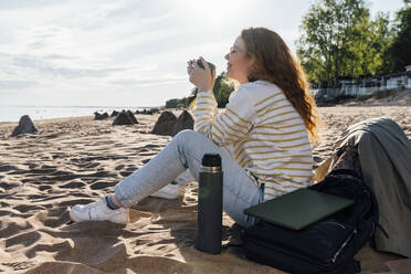 Smiling woman having coffee in insulated cup at beach - VPIF06577