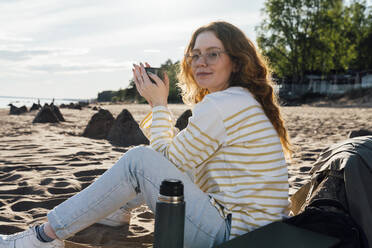 Junge Frau mit Tasse am Strand sitzend - VPIF06578