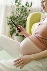 Smiling pregnant woman using smart phone at home - SEAF00977