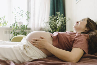 Smiling pregnant woman lying on sofa bed at home - SEAF00987