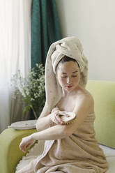 Frau massiert mit Trockenbürste im Wohnzimmer - SEAF00991