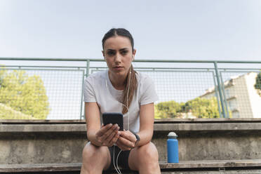 Junge Frau hält Handy und hört Musik über In-Ear-Kopfhörer - FMOF01511