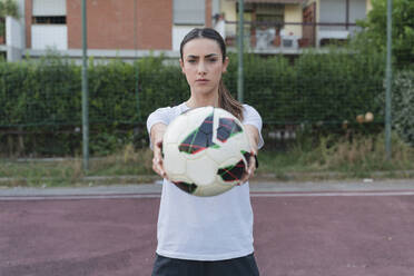 Confident young woman showing ball standing in soccer court - FMOF01521