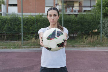 Selbstbewusste junge Frau mit Ball im Fußballfeld stehend - FMOF01521