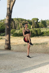 Woman stretching and listening music through wireless headphones on road - FMOF01529