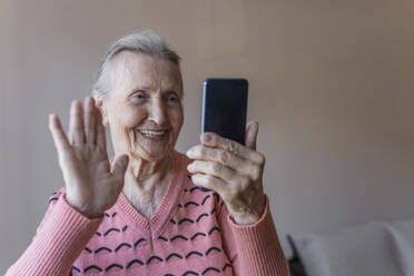 Glückliche Frau winkt bei einem Videoanruf über ihr Smartphone zu Hause - OSF00062