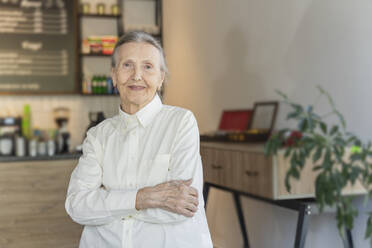 Lächelnde ältere Frau mit verschränkten Armen in einem Café stehend - OSF00085