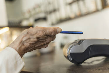 Hand of senior woman paying through smart phone at cafe - OSF00089