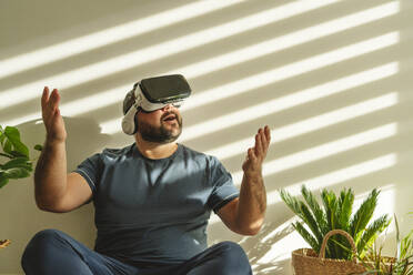 Cheerful man wearing Vr glasses and gesturing in front of wall - OSF00102