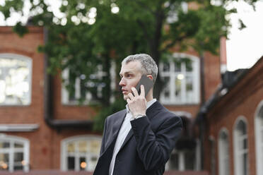 Businessman talking on smart phone in front of buildings - EYAF01927