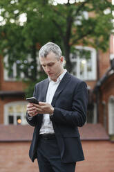 Businessman using smart phone standing on street - EYAF01928