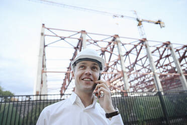 Happy engineer talking on smart phone at construction industry - EYAF01933