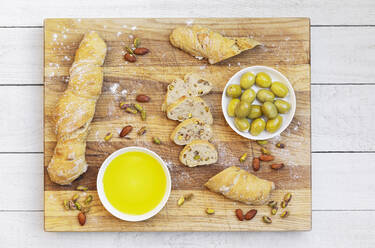 Studioaufnahme einer Schale mit Olivenöl, grünen Oliven und hausgemachtem Pain Paillasse-Brot mit Mandeln und Pistazien - GWF07447