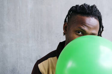 Man holding green balloon in front of face - ASGF02423