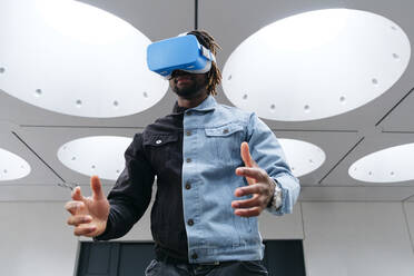 Man gesturing wearing virtual reality headset under illuminated ceiling - ASGF02454