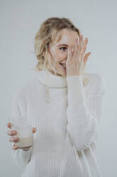 Schüchterne Frau hält ein Glas Pflanzenmilch vor weißem Hintergrund - MFF09125