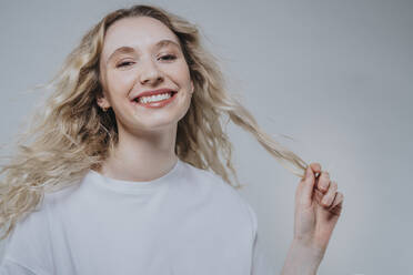 Smiling woman holding blond hair against grey background - MFF09135