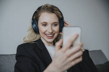 Lächelnde Geschäftsfrau mit Kopfhörern und Blick auf ihr Smartphone - MFF09143