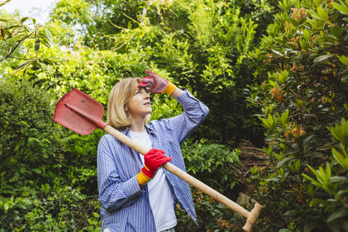 Frau mit Augenschutz trägt Schaufel in der Nähe von Pflanzen im Garten - IHF00910