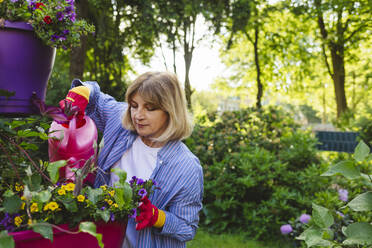 Frau gießt Blumen mit Gießkanne im Garten - IHF00913