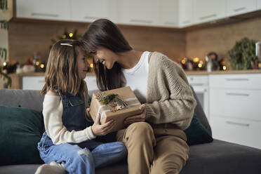 Lächelnde Frau und Tochter, die zu Hause ein Weihnachtsgeschenk miteinander teilen - ABIF01706