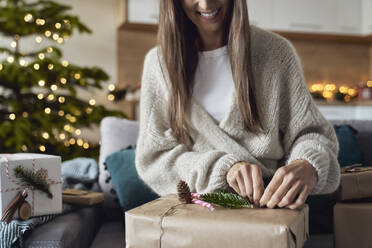 Smiling woman wrapping gift at home - ABIF01716