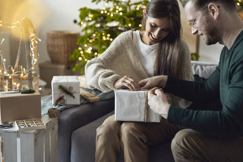 Glückliche Frau mit Mann beim Einpacken von Weihnachtsgeschenken zu Hause - ABIF01719