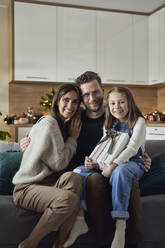 Glückliches Mädchen mit Weihnachtsgeschenk, das mit seinen Eltern zu Hause auf dem Sofa sitzt - ABIF01722